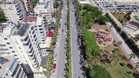 Coastal road. Traffic on seaside avenue. Aerial footage of mediterranean city with palm trees, cars driving on street and residential buildings. Mersin, Turkey
