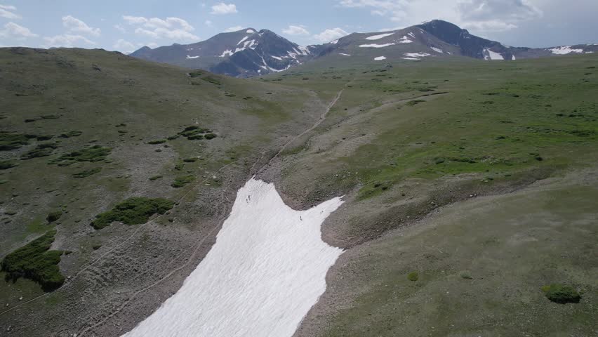 An orbiting 4K drone shot of a group of backcountry skiers preparing to ski down Saint Mary’s Glacier, a semi-permanent snowfield located next to Saint Mary’s Lake in Colorado, USA.