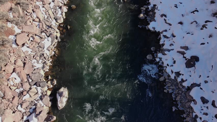 A spectacular 4K drone shot of the Colorado River running adjacent to I-70 and an old railroad, through the Rocky Mountains of Colorado, during the winter season.