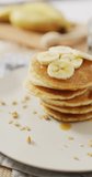 Vertical video of stack of american style pancakes topped with banana slices. home cooking sweet treat, food, flavour and nutrition.