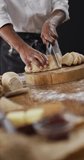 Vertical video of midsection of african american baker slicing loaf of white bread on chopping block. healthy food, diet and nutrition.