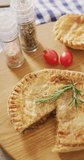 Vertical video of baked savoury pie missing slice, with rosemary, salt, pepper and tomatoes on table. home cooked food, diet and nutrition.