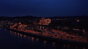 Palma Cathedral Catedral de Santa María de Palma de Mallorca flying around with illuminated streets with night traffic on sea embankment during sunset evening time blue hours 4K footage.