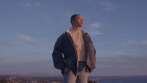 Diverse young adult with shaved head stands above city at golden hour Video stock