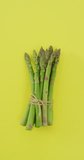 Vertical video of fresh stalks of asparagus tied with rustic string on yellow background. fresh and organic vegetable produce.