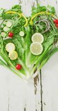 Vertical video of fresh tomatoes and green vegetables forming heart on white rustic background. fresh and organic vegetable produce.