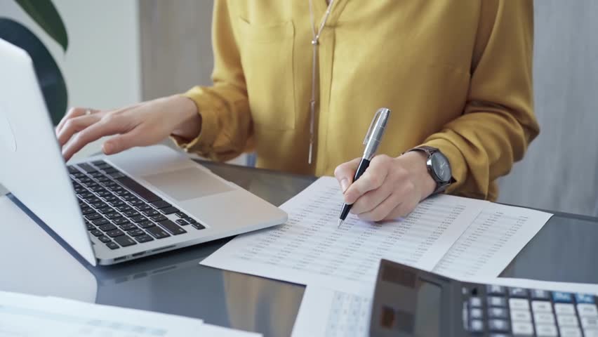Professional business woman in yellow blouse is working on financial reports. Close-up of a woman's hands as she works on finance documents and laptop computer. Audit - Powered by Shutterstock - Get 15% off with code: PIKWIZARD15