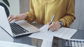 Professional business woman in yellow blouse is working on financial reports. Close-up of a woman's hands as she works on finance documents and laptop computer. Audit