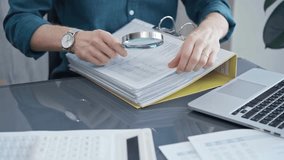 Businessman or professional auditor is analyzing data sheets. Close-up of an bookkeeper's hand with magnifying glass inspecting financial reports. Business audit and taxes