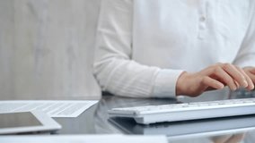 Close-up of a person's hands typing on a white keyboard with papers in background. Business people concept