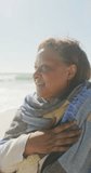 Vertical video of happy senior african american woman at beach. spending free time at beach holiday.