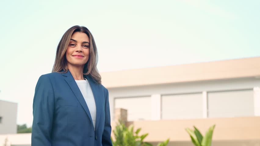 Happy confident mature older Latin business woman real estate agent, saleswoman realtor or new property buyer modern villa owner standing outside villa or country house outdoors. Portrait. Royalty-Free Stock Footage #3469333993