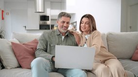 Happy middle aged older couple using laptop computer relaxing on couch at home. Smiling mature man and woman talking with device doing ecommerce shopping sitting on sofa in living room. - Powered by Shutterstock - Get 15% off with code: PIKWIZARD15