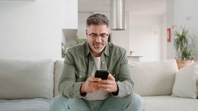 Smiling relaxed senior mature middle aged man holding cell mobile phone using smartphone sitting at home on couch in modern living room, scrolling social media, buying online, texting messages. - Powered by Shutterstock - Get 15% off with code: PIKWIZARD15