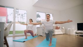 Fit sporty middle aged couple doing yoga at home. Senior healthy mature man and woman standing in yoga pose enjoying morning stretching exercises in modern house living room. - Powered by Shutterstock - Get 15% off with code: PIKWIZARD15
