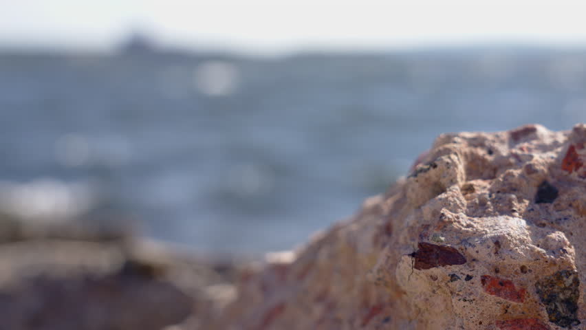 Rack focus from rocks on shore to distant pulp mill factory on the other side of a large body of water, on a windy summer day