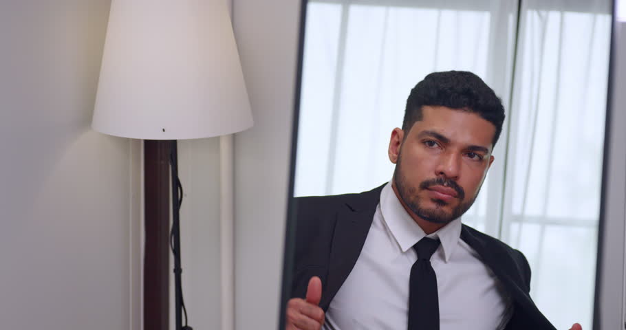 Handsome young businessman gets dressed in front of the mirror before going to work.