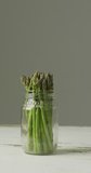 Vertical video of fresh stalks of asparagus in glass jar on grey background. fresh and organic vegetable produce.