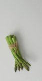 Vertical video of fresh stalks of asparagus tied with rustic string on grey background. fresh and organic vegetable produce.