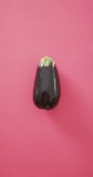 Vertical video of high view of fresh aubergine on pink background. fresh and organic vegetable produce.
