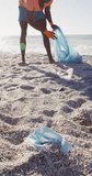 Vertical video of african american man segregating waste at beach. spending free time at beach holiday.