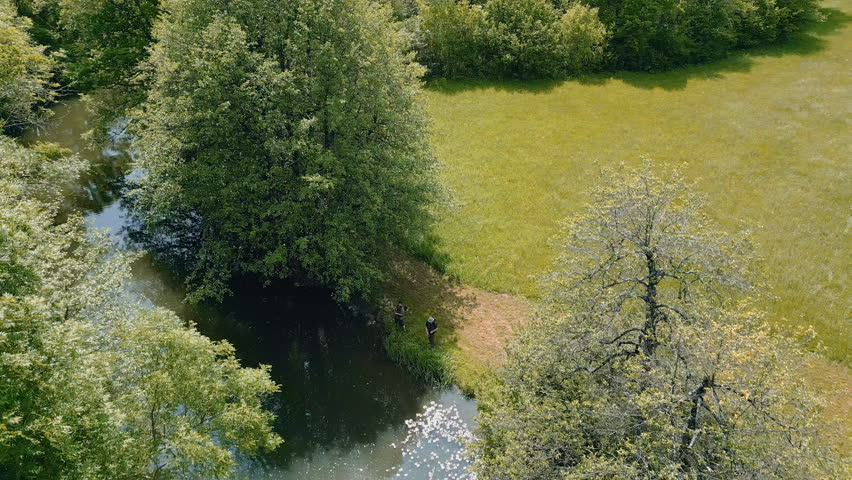 Picturesque scenery of a river shore in summer and two fishermen peacefully fishing in calm water, aerial reveal shot. Nature getaway concepts.