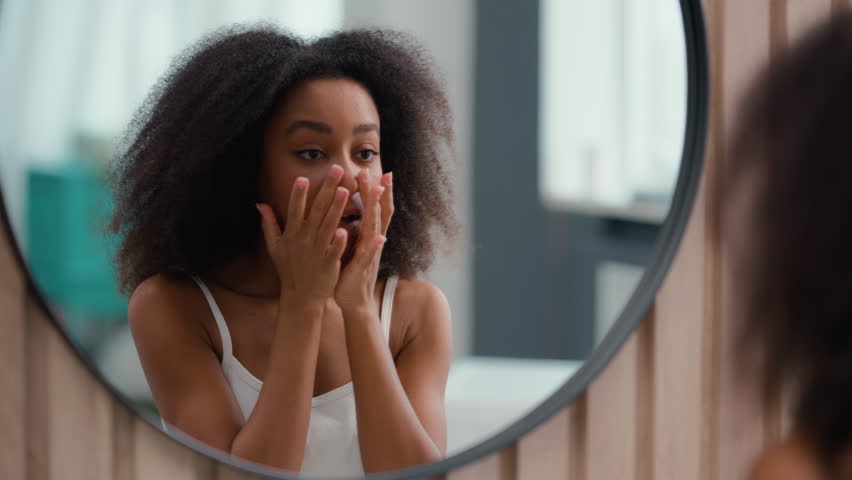 Mirror reflection in bathroom pretty attractive woman African American girl female skin care looking touching face using cream moisturize beauty cosmetic lips moisturizing procedure facial massage