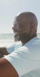 Vertical video of happy senior african american man at beach. spending free time at beach holiday.