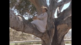 Old film clip of a woman sitting in a tree with a sun hat