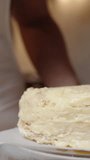 Vertical video. The woman spreads the cream in a circular motion on the Napoleon cake using a spoon. Close-up view.