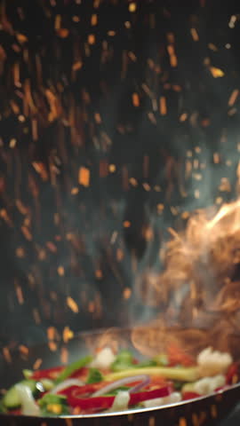 Closeup of chef preparing and throwing vegetable mix on frying pan on fire. Preparation fresh appetizing food. Vegetables flying in slow motion. Healthy vegetarian food cooking. Vertical video
