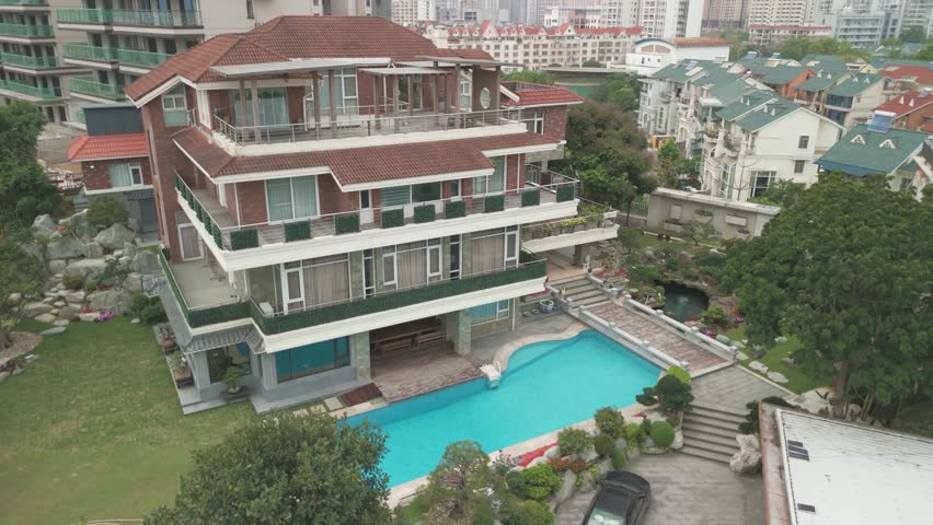 Flying from a drone over a beautiful house with a swimming pool and a gazebo on a sunny day. The first line of residential buildings on the coastline. Nanning, China