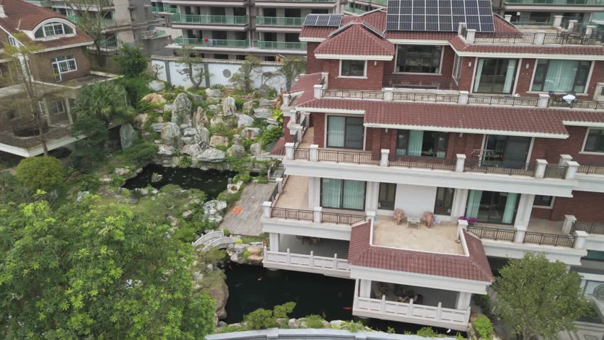 Flying from a drone over a beautiful house with a swimming pool and a gazebo on a sunny day. The first line of residential buildings on the coastline. Nanning, China