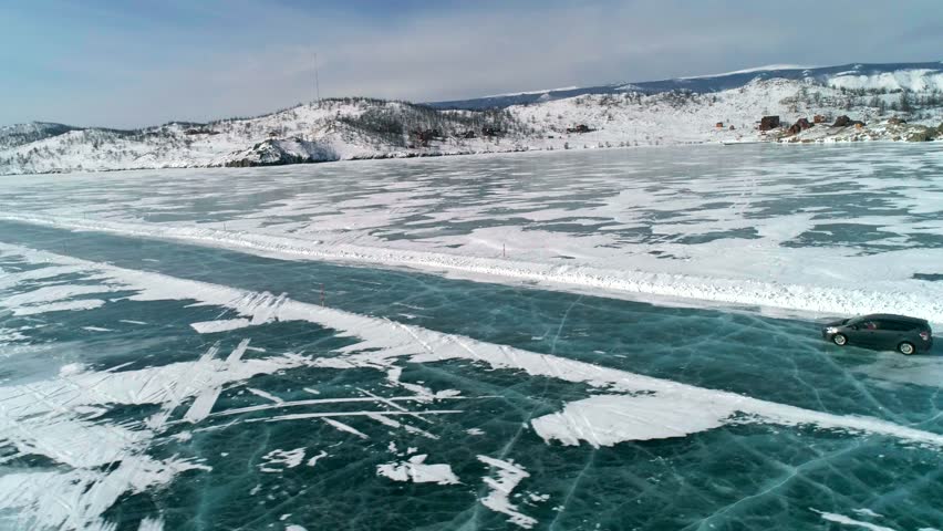 Aerial side view on a car driving on an ice road on frozen Baikal. Winter landscape of lake Baikal. Drone follows the car.