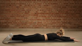 This athlete in a black outfit extends into a superman pose on the mat, effectively engaging her back muscles and core for a comprehensive strengthening session in a brick-textured gym environment. - Powered by Shutterstock - Get 15% off with code: PIKWIZARD15