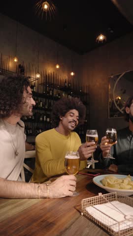 Vertical video of a A group of colleague workers toast with beer in the restaurant bar after work at the pub happy hour. Happy friends having fun together drinking alcohol indoors.