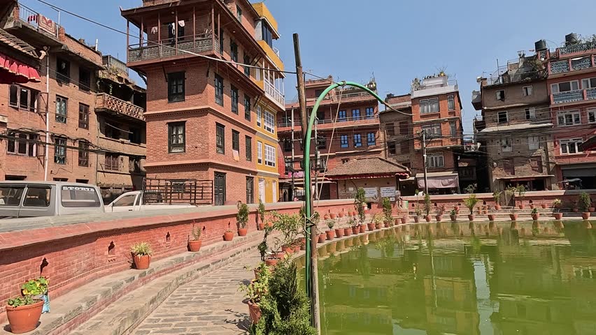 vibrant green Bholachhe Pond in the core of Bhaktapur, Nepal. Plant pots and brick buildings surrounding the lake.