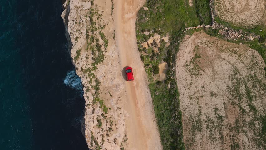 Driving a car at cliff edge on Malta island. Scenic nature seaside. Aerial drone rock formation