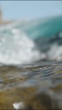 Vertical video. Close-up shot of a sea wave with transparent water covering the camera and bubbles appearing throughout the frame, in slow motion.