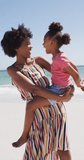 Vertical video of happy african american mother with daughter at beach. family spending time together.