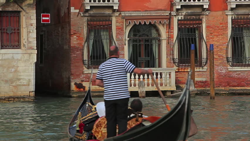 VENICE - MAY 2012: Gondolier steering through canal with passenger.
