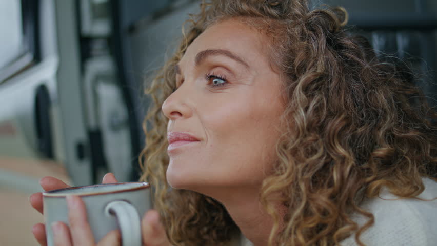 Closeup tourist holding cup with hot beverage sitting motorhome stairs. Portrait relaxed middle-aged woman looking camera posing with coffee mug at trailer. Carefree lady enjoy enjoy morning at camper