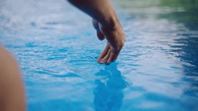 Close up of hydrated female hand trailing in clear, reflective water of an exotic infinity pool, surrounded by rich tropical plants. Woman enjoys serene luxury resort atmosphere, relaxation vibe. - Powered by Shutterstock - Get 15% off with code: PIKWIZARD15