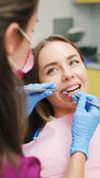 The dentist is performing dental treatment on a female patient with a flawless smile, vertical video