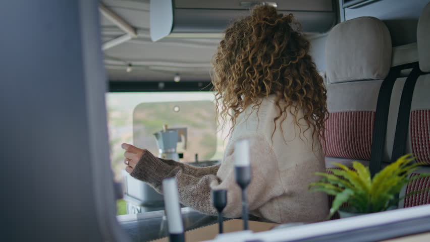 Happy female tourist posing campervan at weekend journey close up. Attractive curly woman sitting trailer kitchen looking camera view from window. Dreamy middle-aged lady relaxing at motorhome alone.