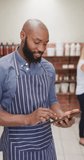Vertical video of smiling african american in apron using tablet in organic store. eco shopping, organic farm and fresh organically grown vegetables.