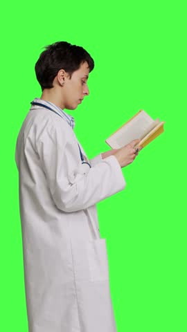 Profile Medic specialist reading a healthcare literature book to develop her medical expertise in the industry, stands against greenscreen backdrop. Clever doctor in white coat enjoys lecture. Camera Royalty-Free Stock Footage #3469943343