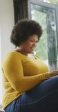 Vertical video of plus size biracial woman using laptop at home. spending active time at home and body inclusivity.