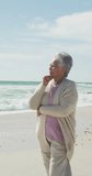 Vertical video of happy biracial woman alone on sunny beach. healthy, active retirement beach holiday.
