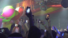 Crop man using smartphone to take video of concert alive in spacious dark hall with flashing lights. Many phones make a concert.